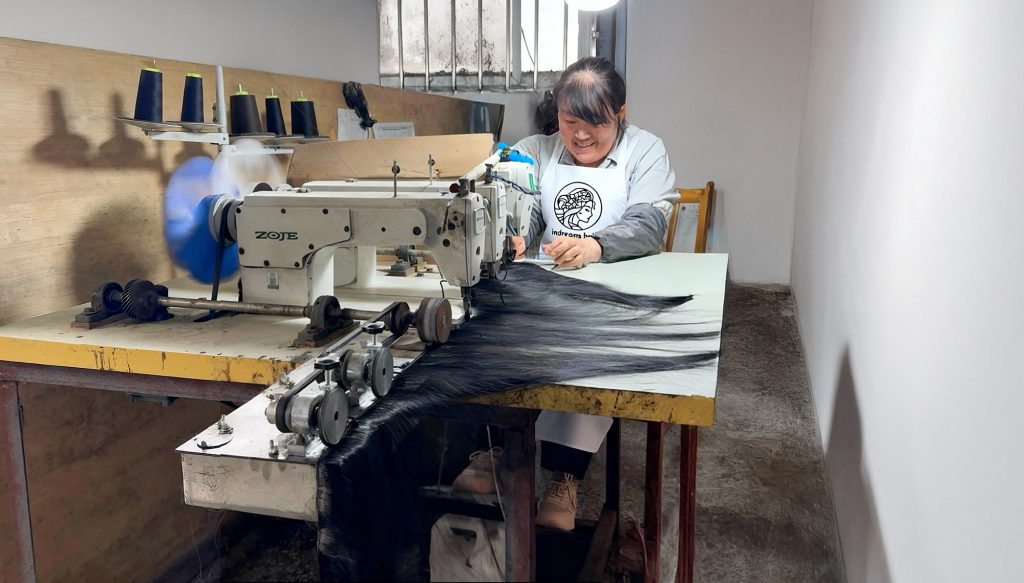 A skilled worker at indreams hair factory is using a sewing machine to sewing human hair weft for hair extensions production.