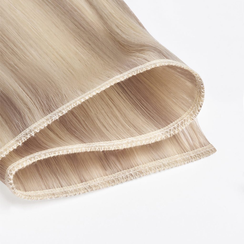Extreme close-up of premium 100% virgin remy cuticle human hair machine weft extensions with reinforced double stitching in highlight blonde for B2B wholesalers and salons.